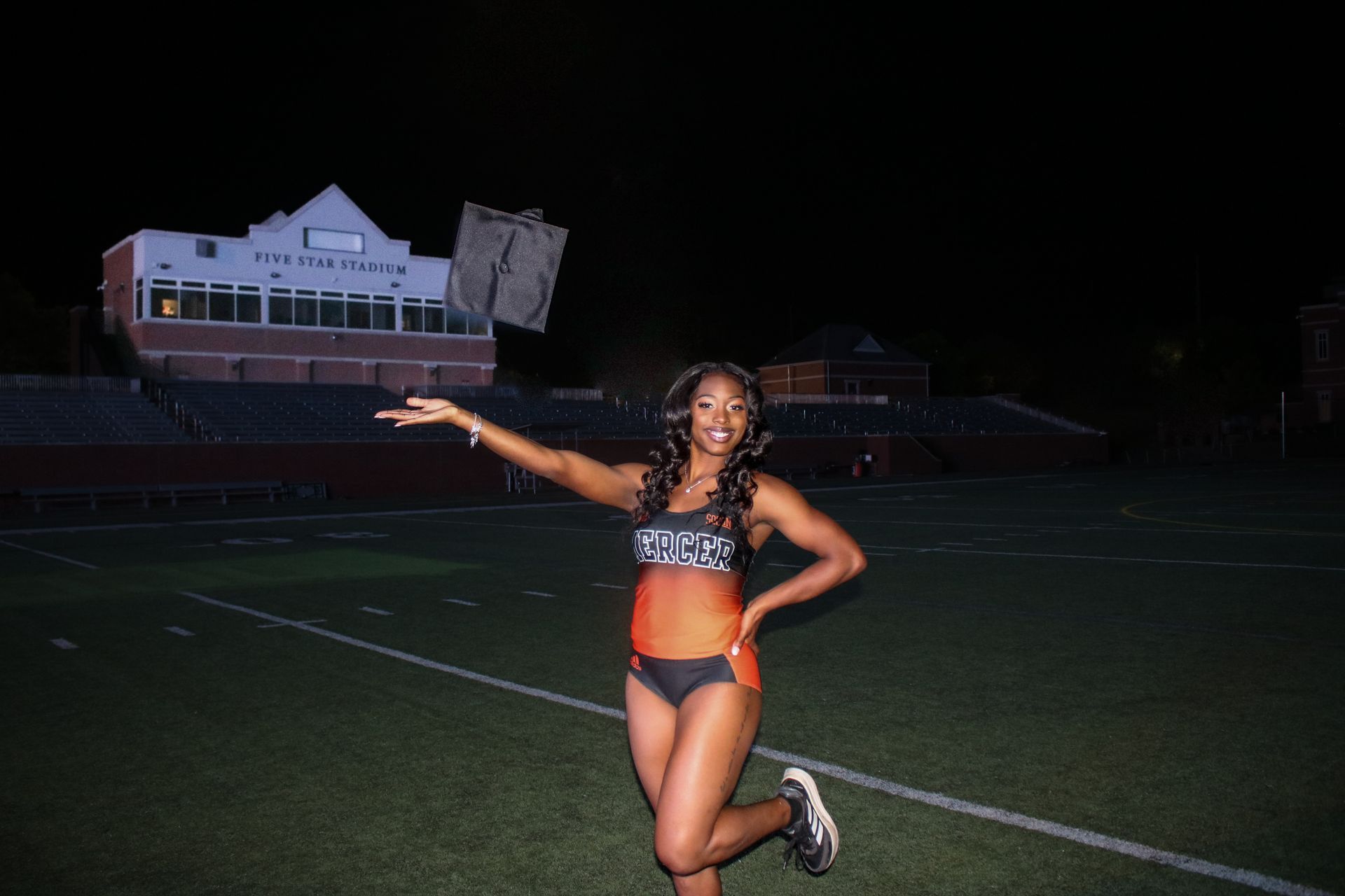 A woman in a bikini is standing on a football field at night.