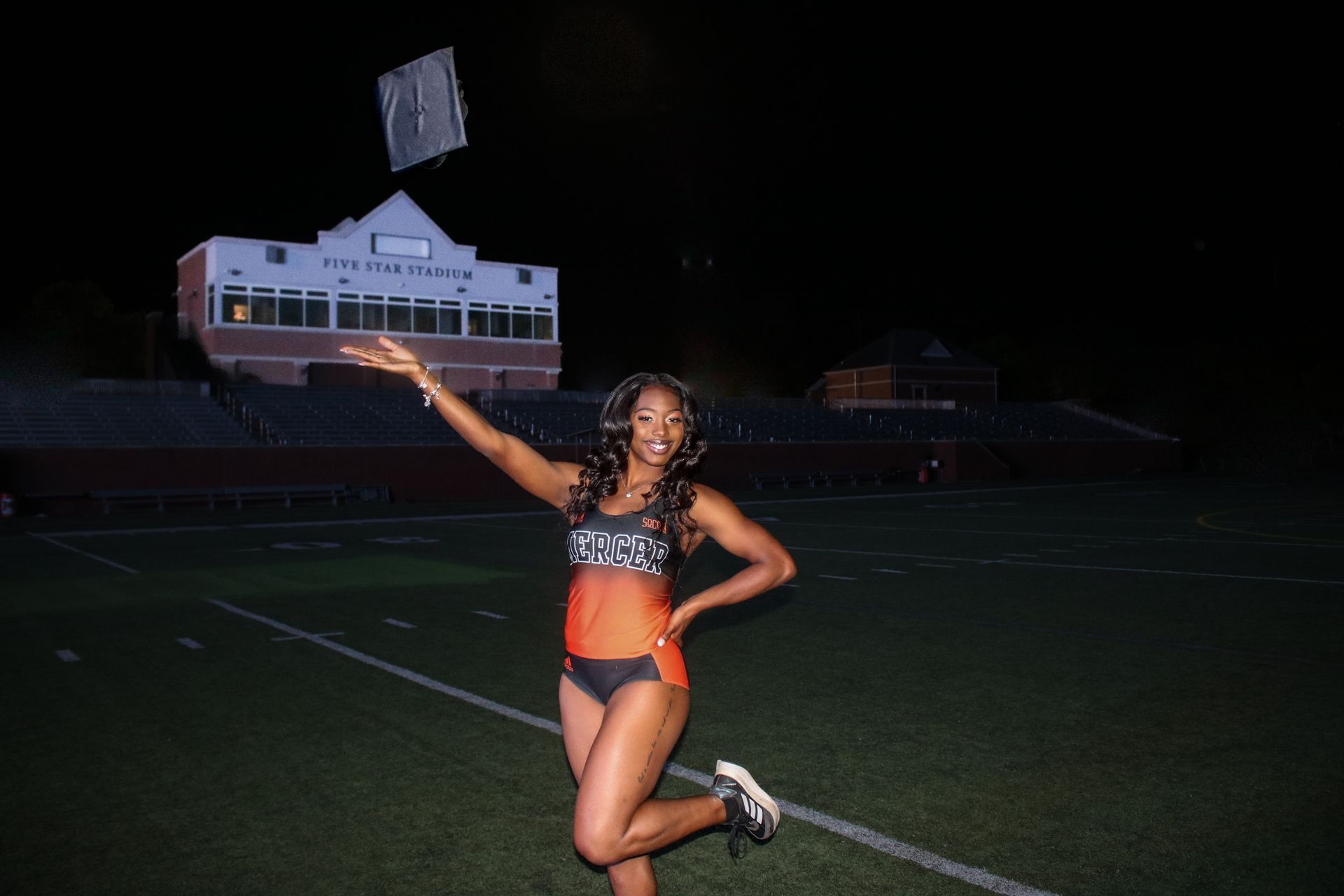 A woman in a bikini is kneeling on a football field at night.