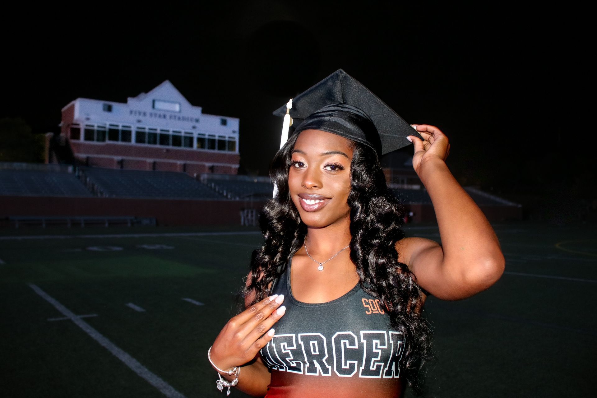 A woman wearing a graduation cap and gown is standing on a football field.