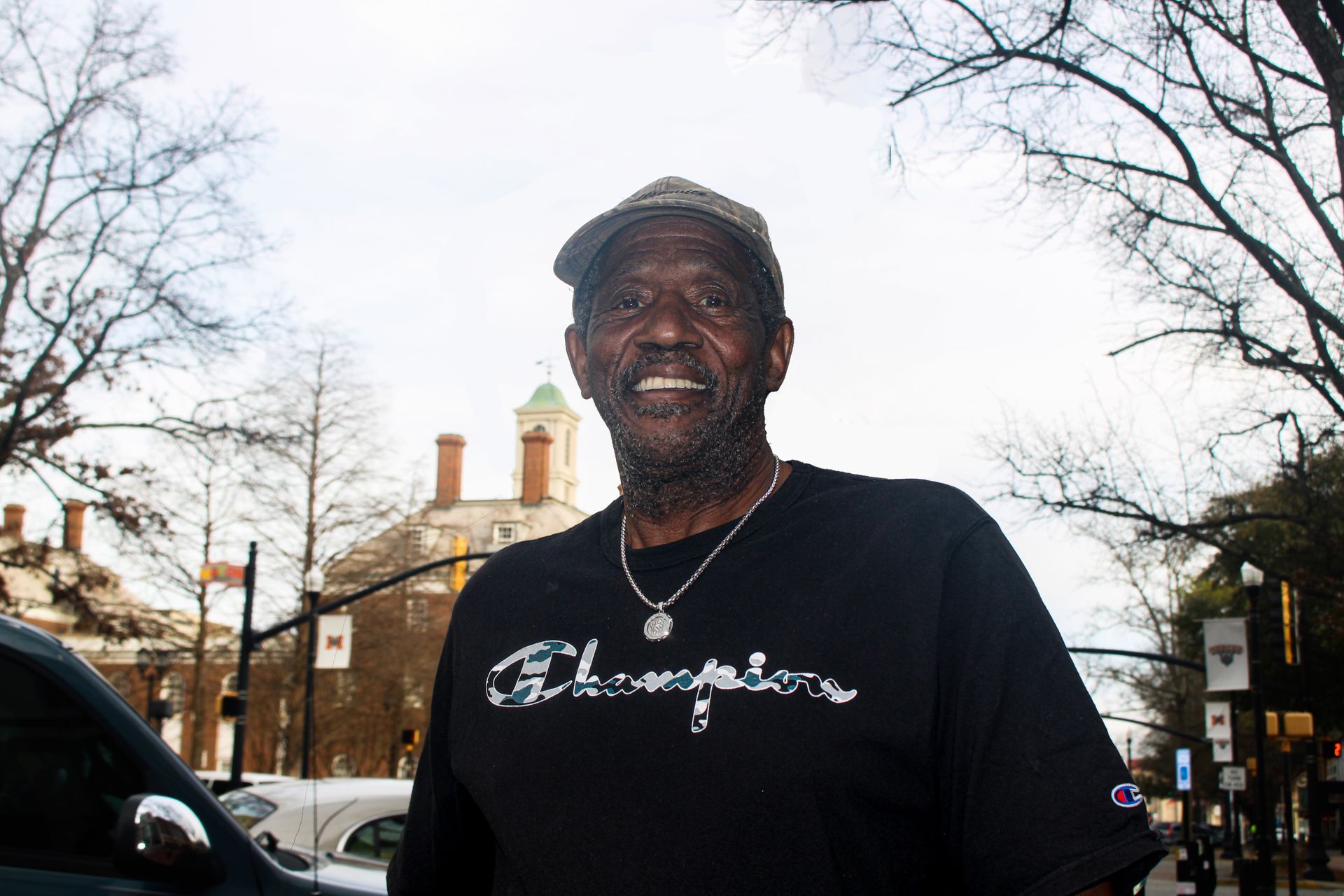A man wearing a black champion shirt is standing in front of a car