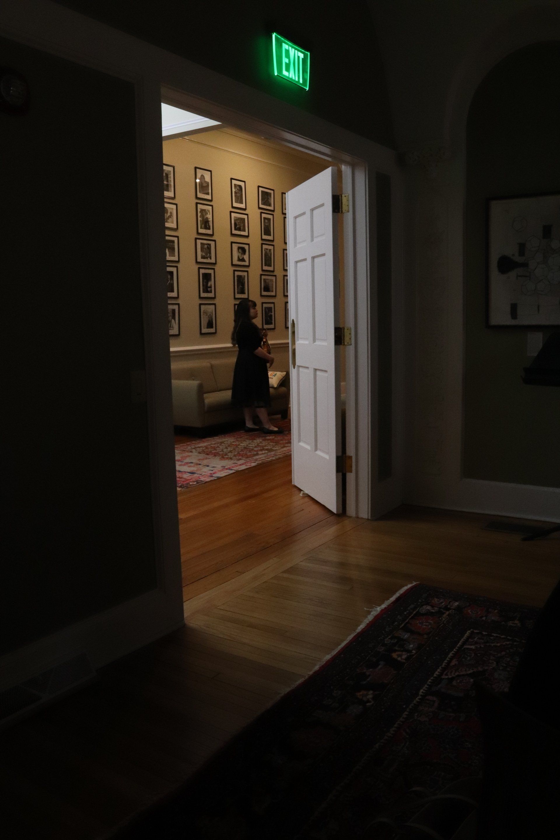 A green exit sign is above a doorway in a dark room