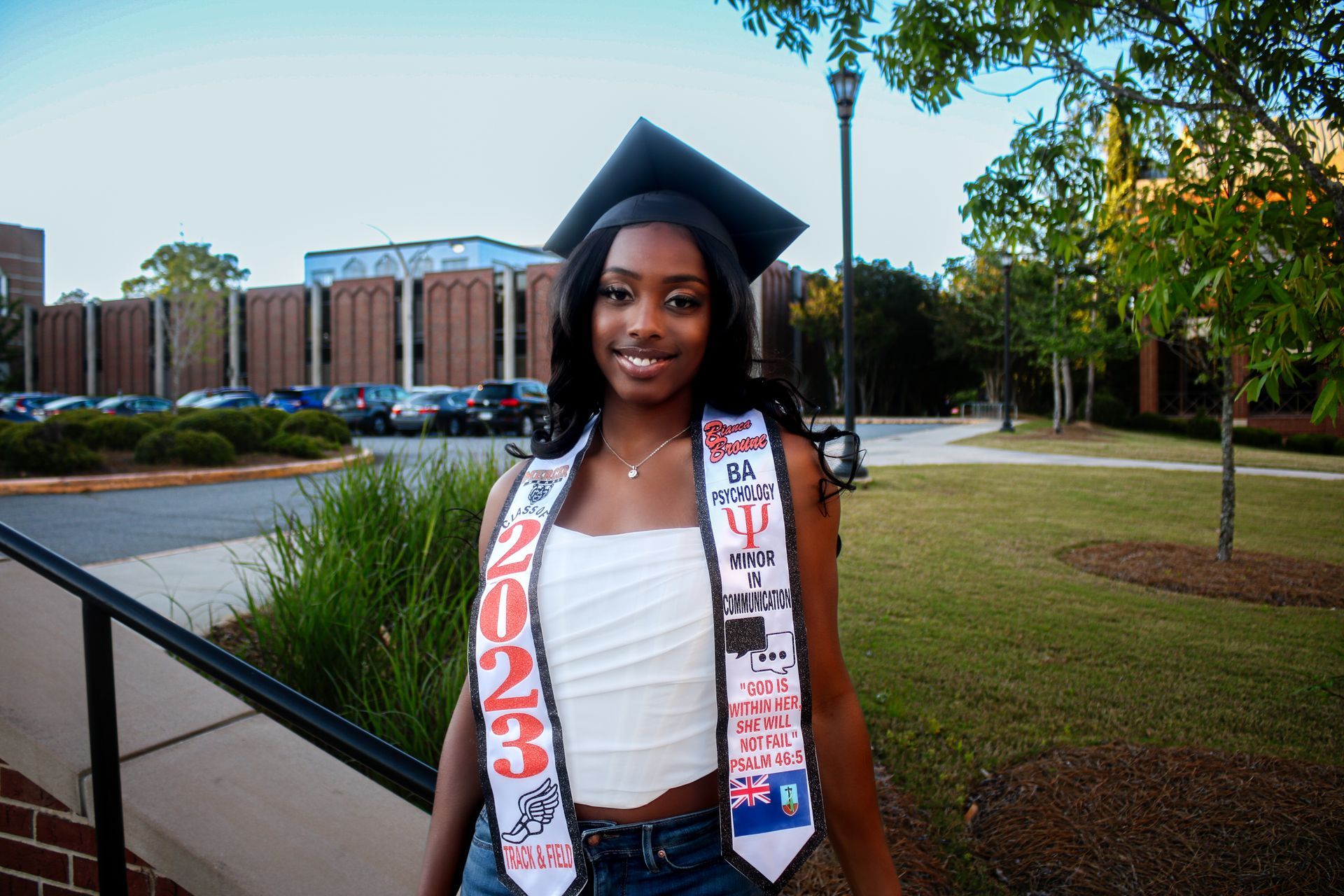 A woman wearing a graduation cap and gown is standing in front of a building.
