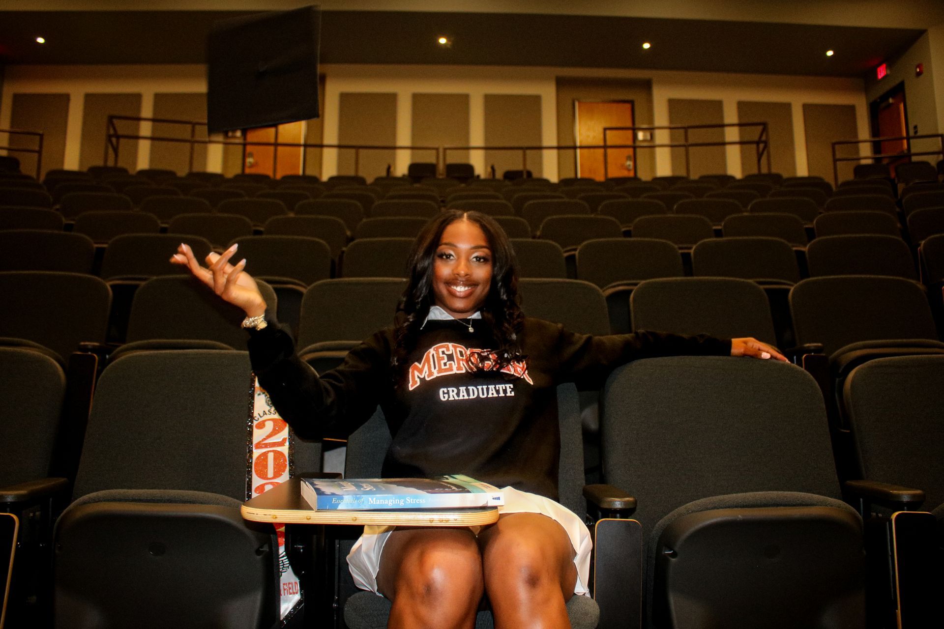 A woman is sitting in an auditorium with her arms outstretched