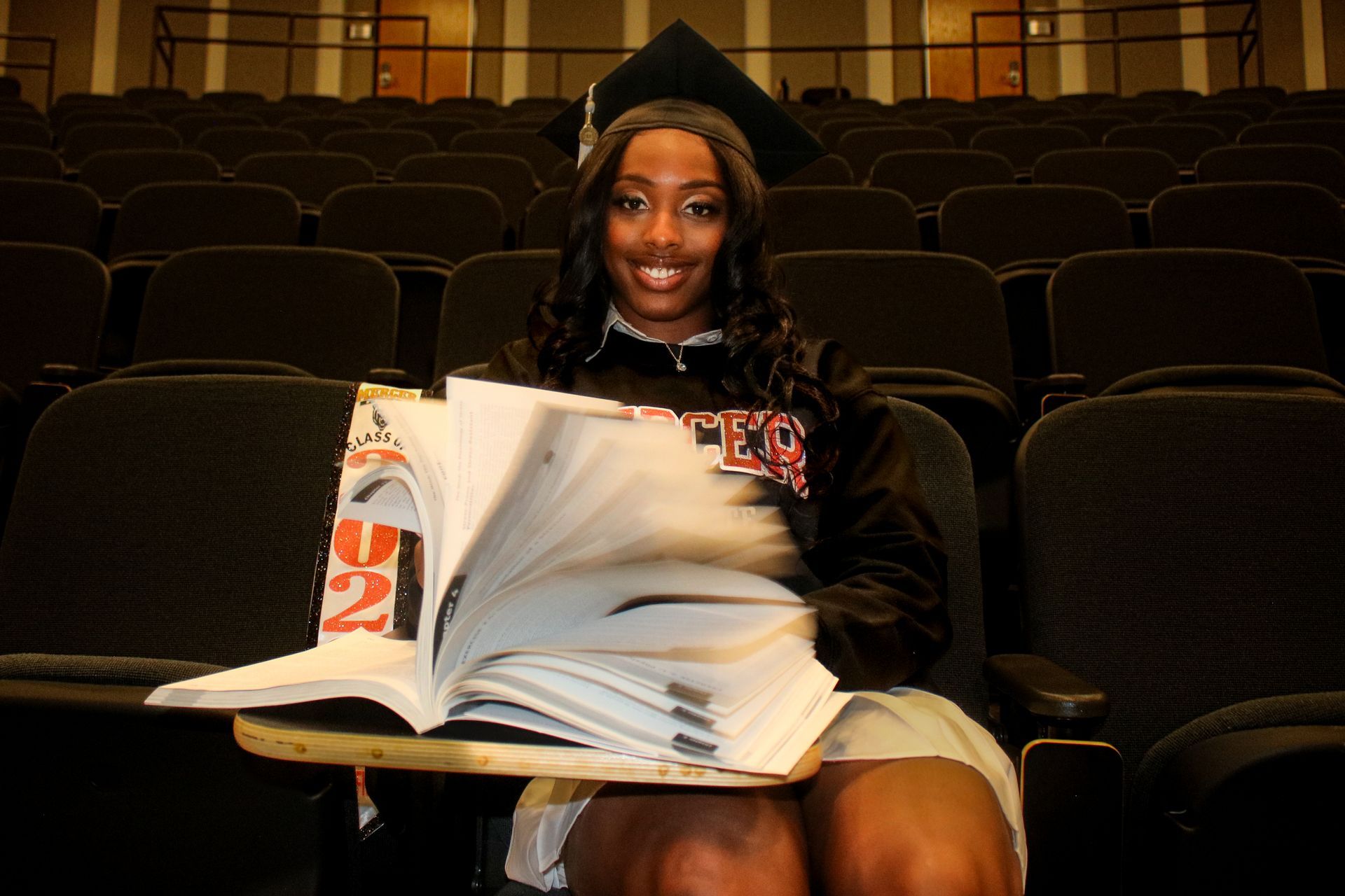 A woman in a graduation cap and gown is holding an open book