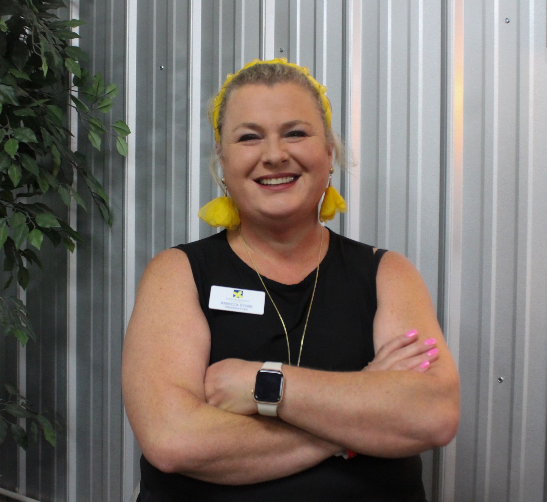 A woman wearing a black shirt and a name tag smiles with her arms crossed