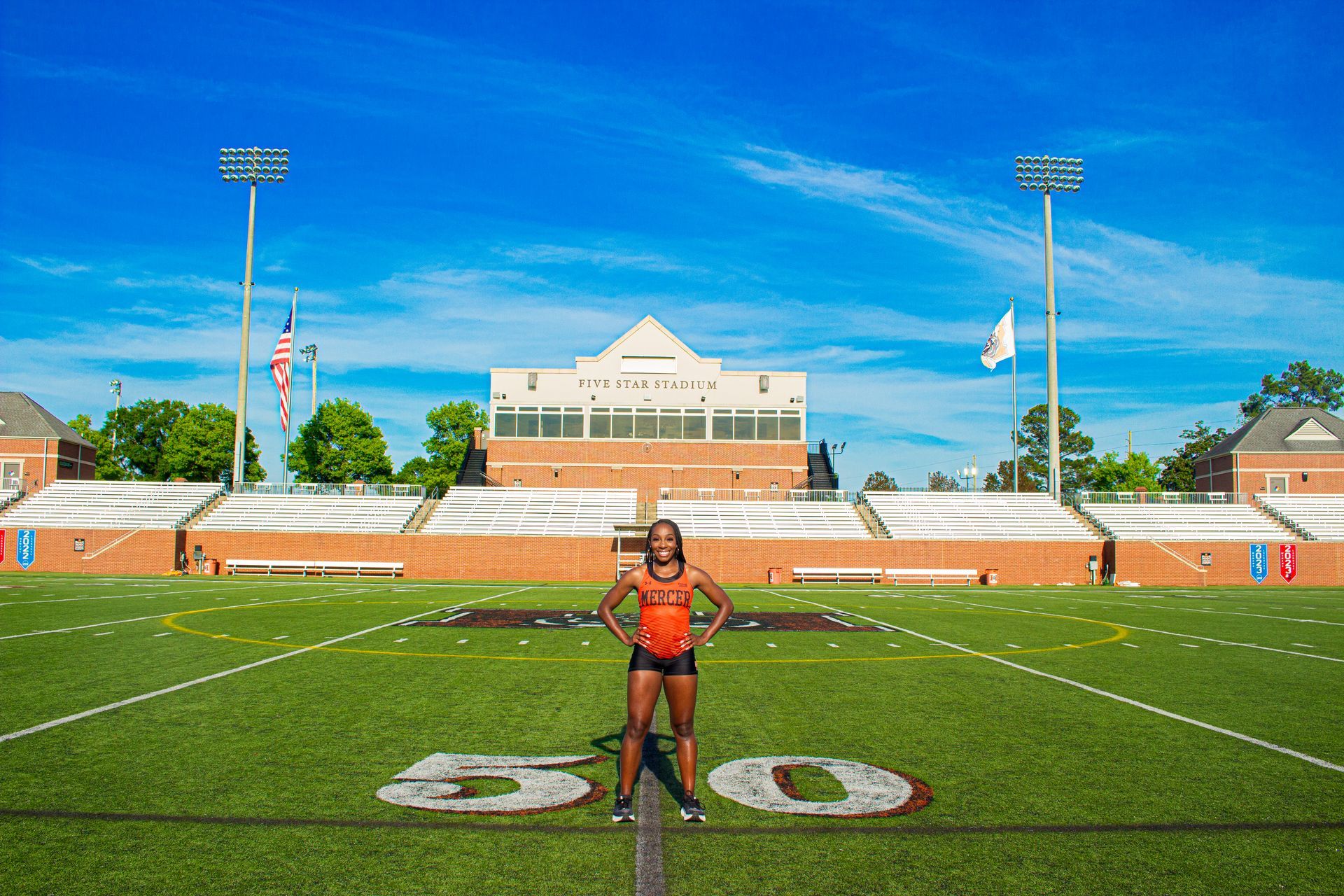 A woman is standing on a football field in front of a stadium.