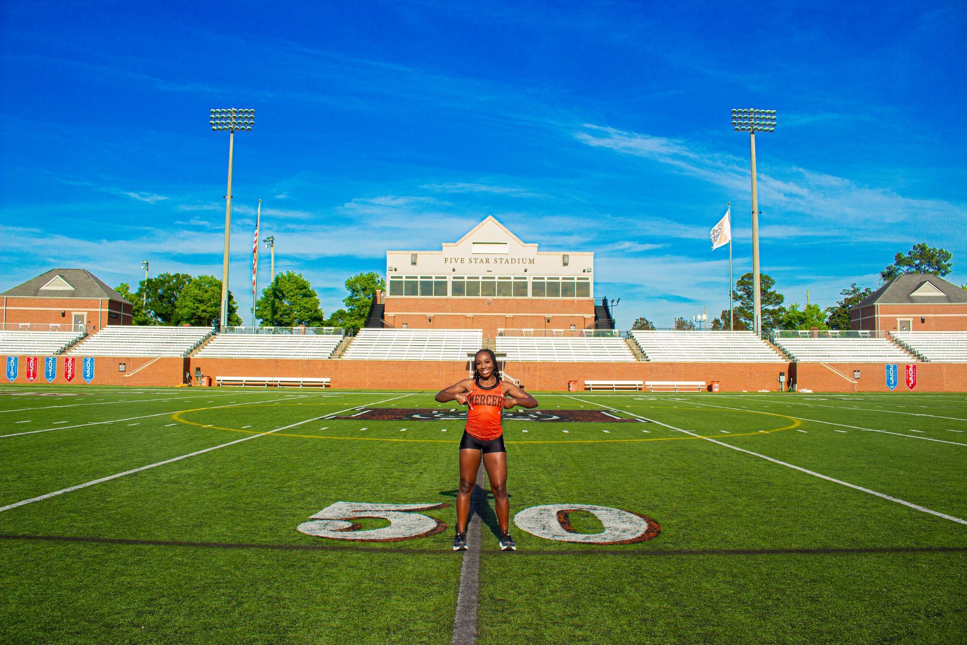 A woman is standing on a football field in front of a stadium.