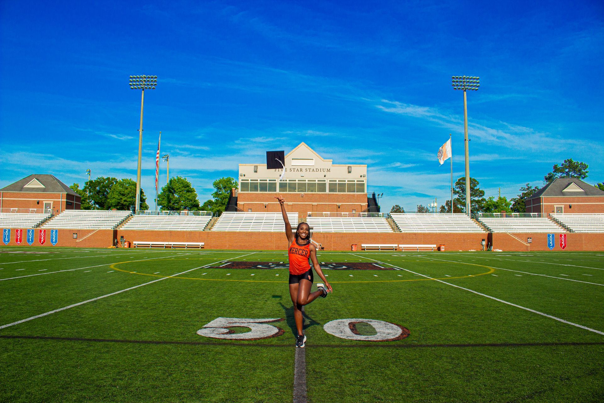 A woman is standing on a football field with her arms in the air.