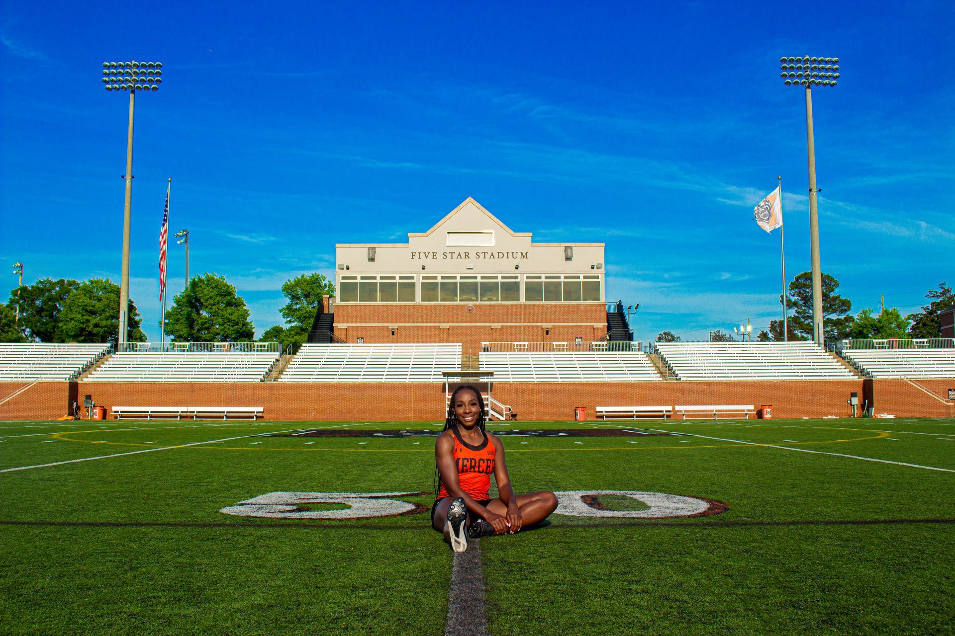 A person is sitting on the grass in front of a stadium.