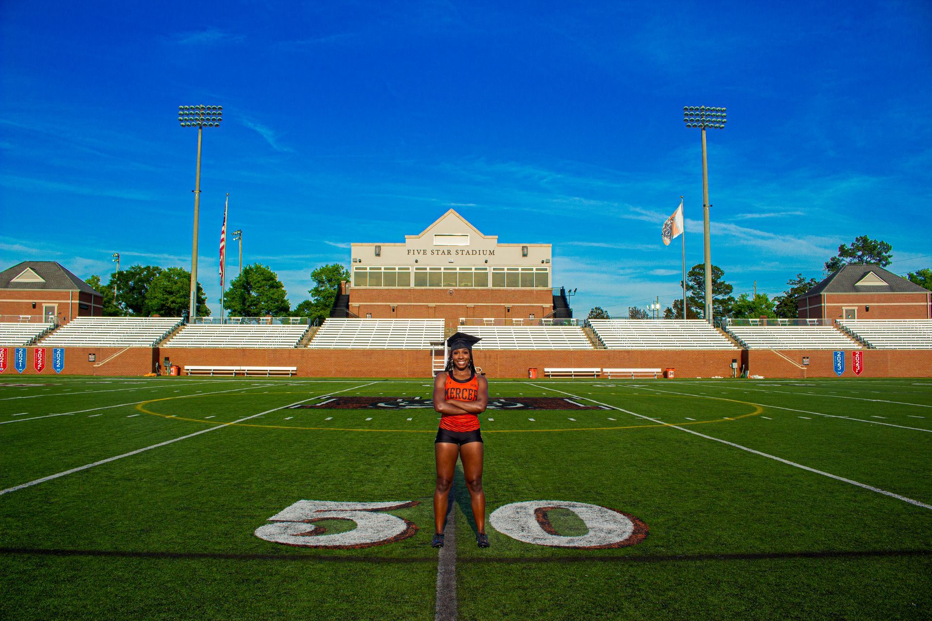 A woman is standing on a football field in front of a stadium.