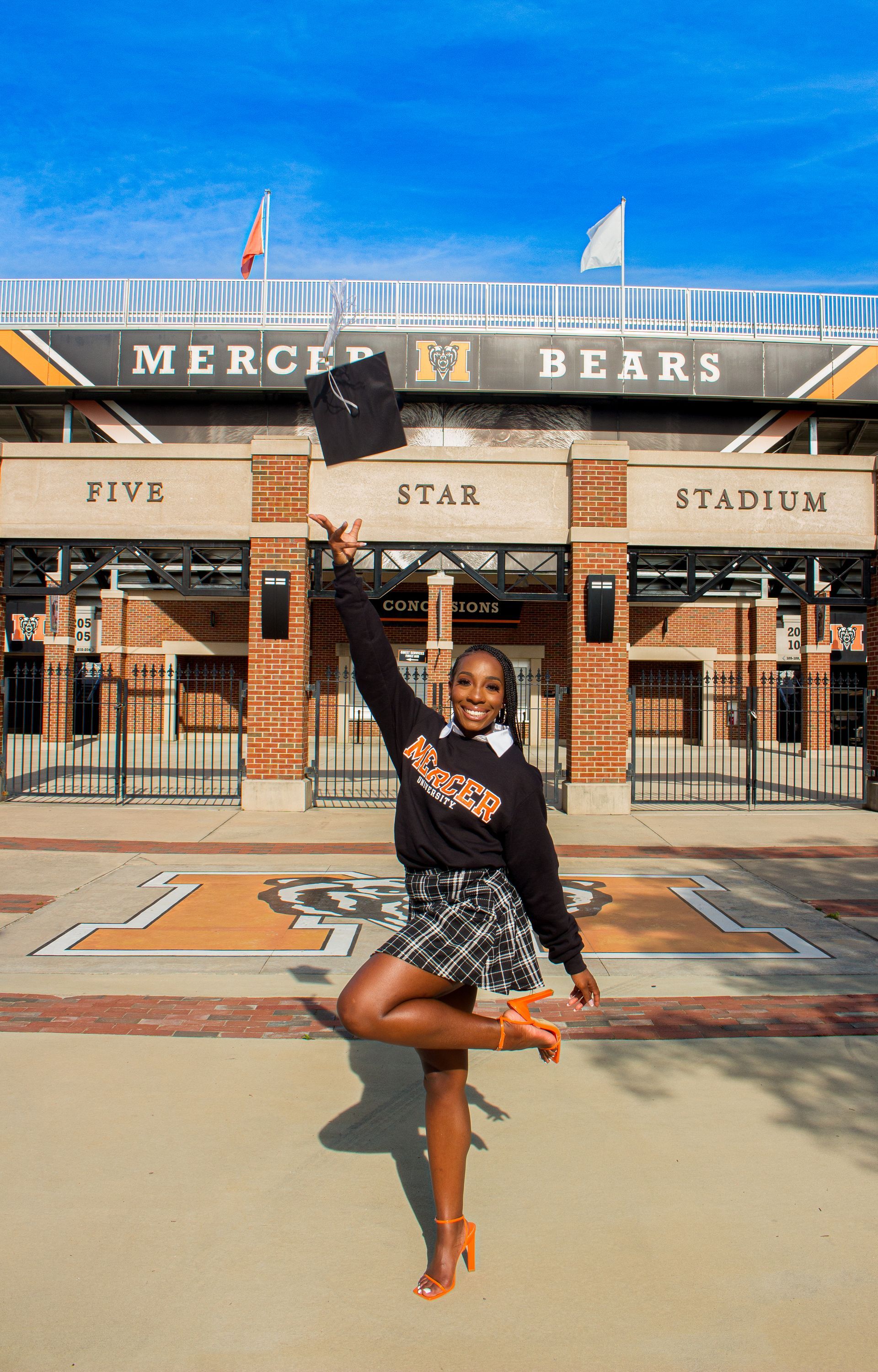 A woman is standing in front of a stadium holding a cap in the air.