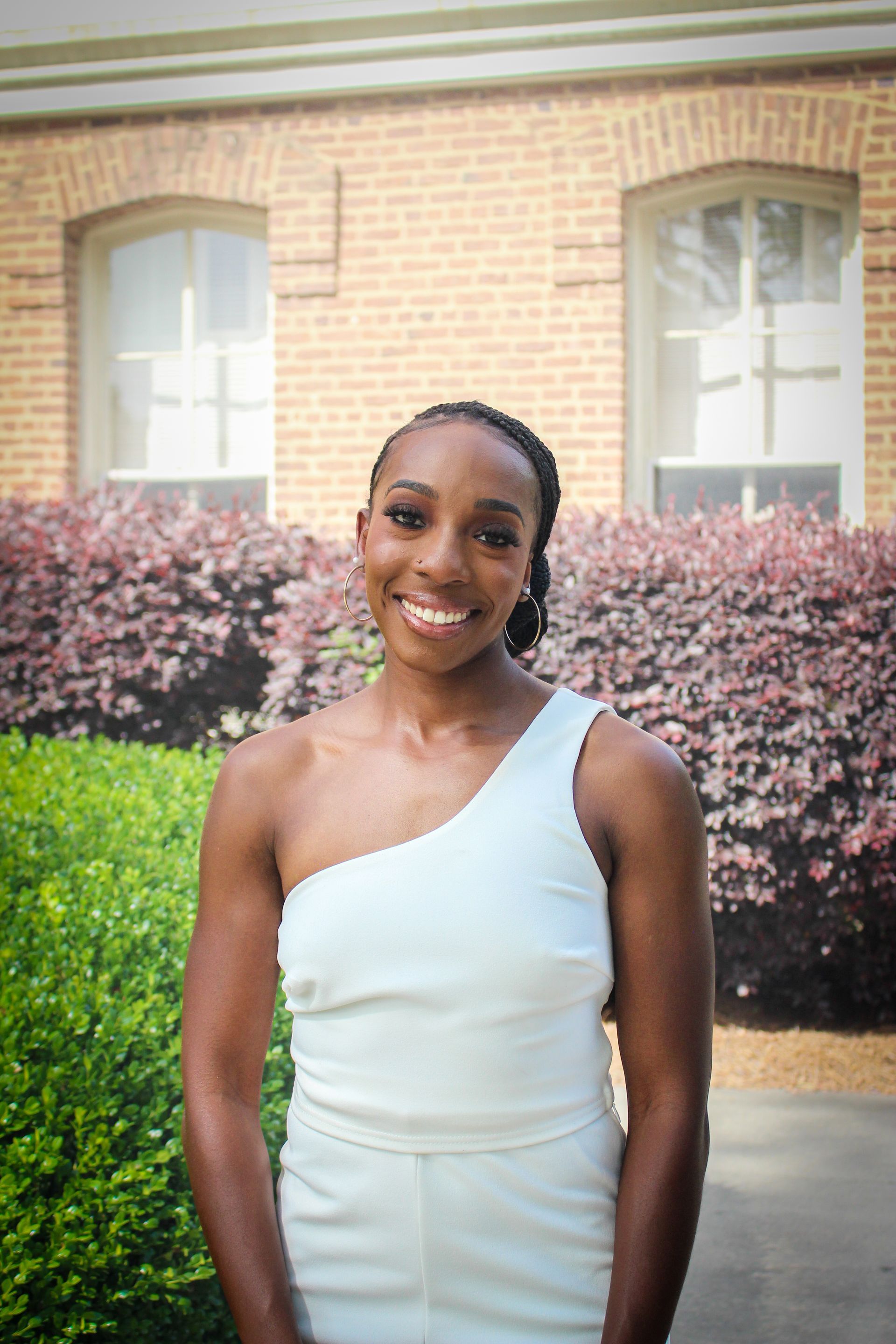 A woman in a white dress is standing in front of a brick building.