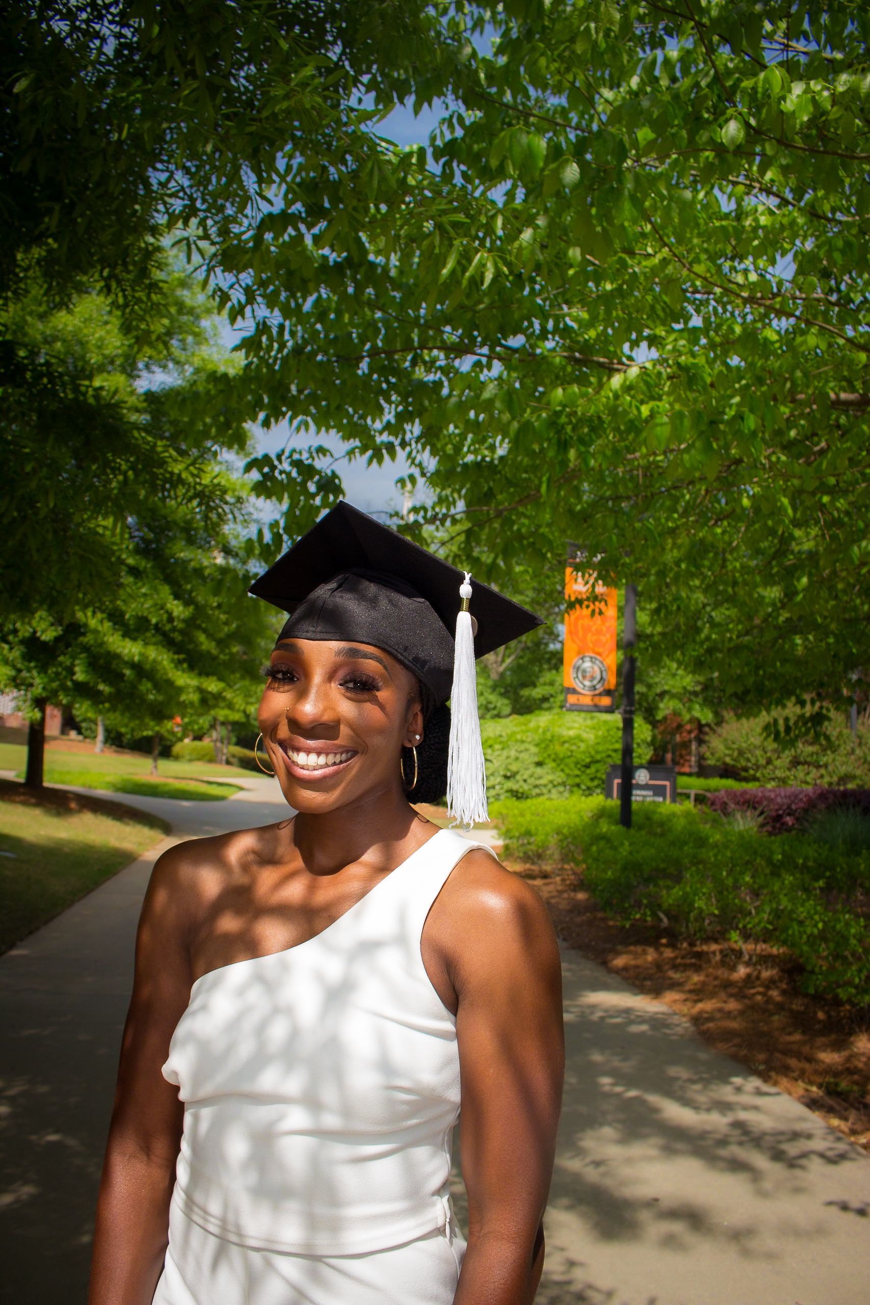 A woman wearing a graduation cap and gown is standing on a sidewalk.