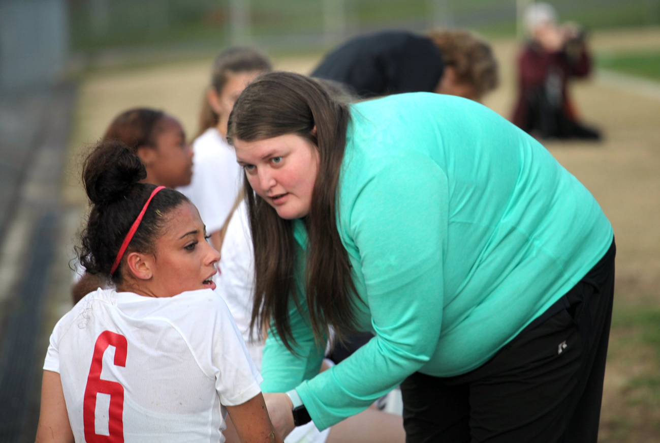 A woman in a green sweater is talking to a girl in a white shirt with the number 6 on it.