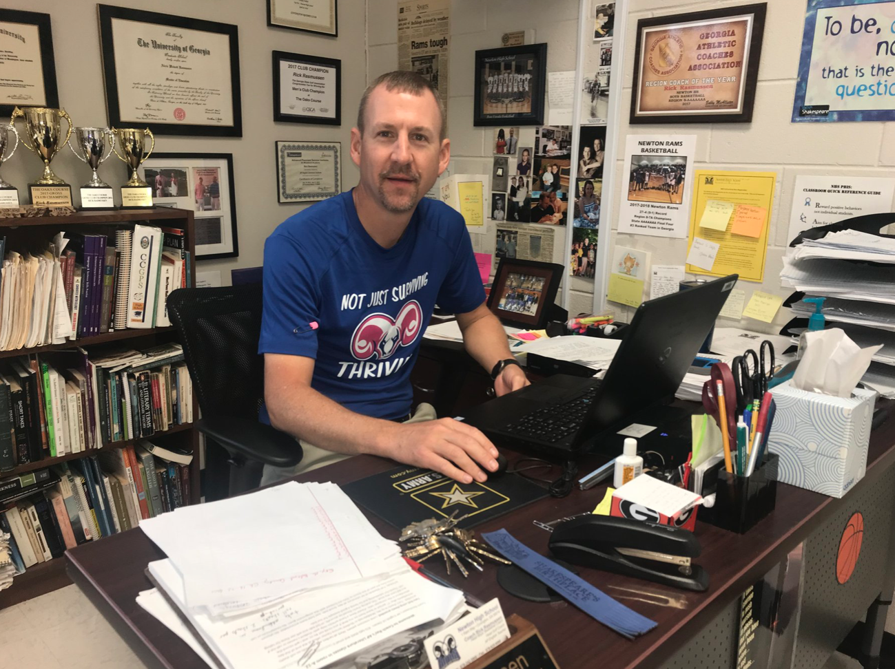 A man in a blue shirt is sitting at a desk with a laptop