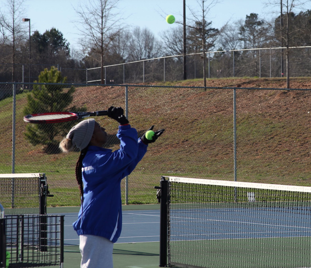 A man in a blue jacket is hitting a tennis ball