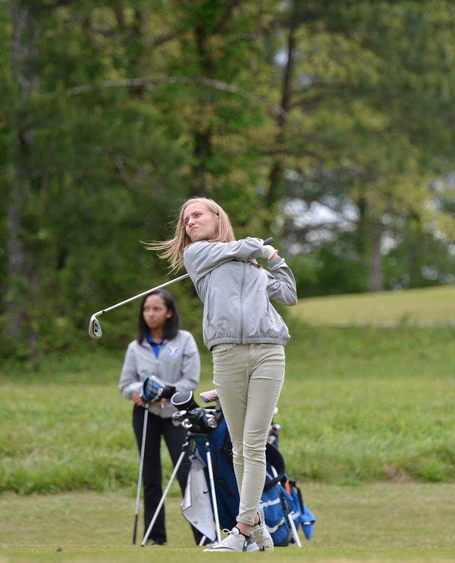 A woman is swinging a golf club on a golf course.