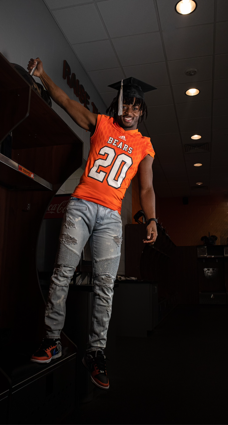 A man wearing a graduation cap and gown is standing in a dark room.