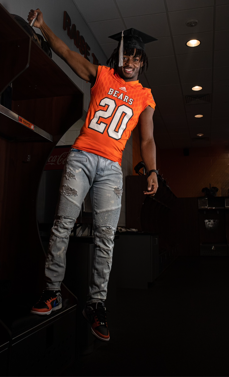 A man wearing a graduation cap and gown is jumping in the air.