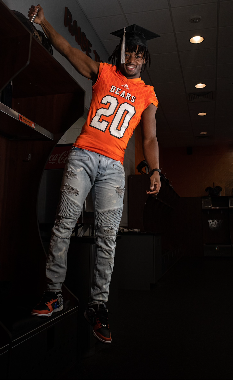 A man wearing a graduation cap and gown is jumping in the air.