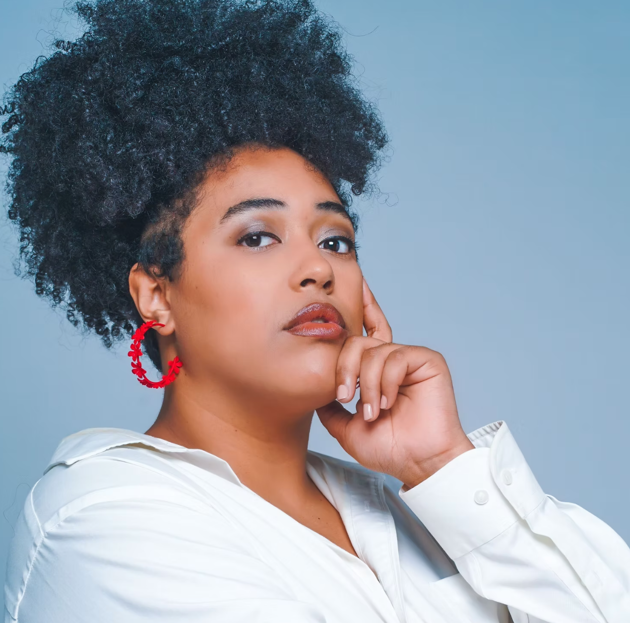 A woman with curly hair is wearing red hoop earrings