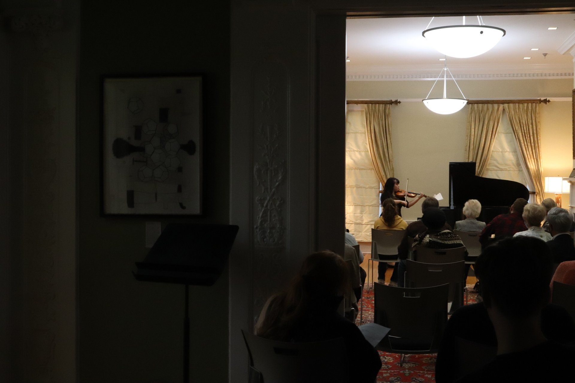 A group of people are sitting in a dark room watching a woman play a violin
