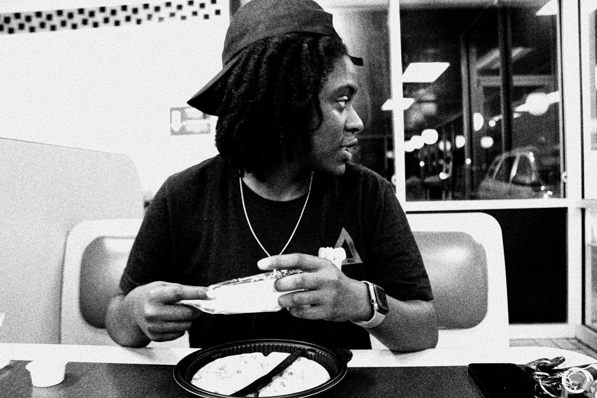 A black and white photo of a man sitting at a table eating a pizza.
