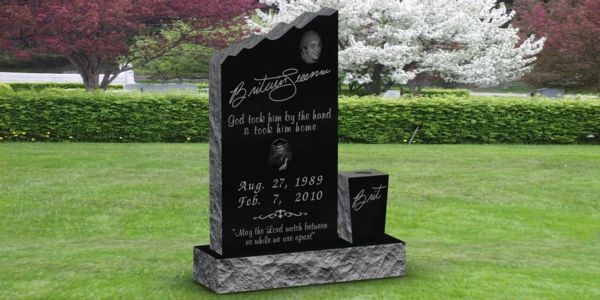 A black gravestone is sitting in the middle of a lush green field.