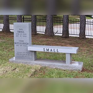A gravestone with a bench in front of it in a cemetery.