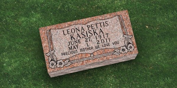 A gravestone for leona pettis kasiska is sitting on top of a lush green field.