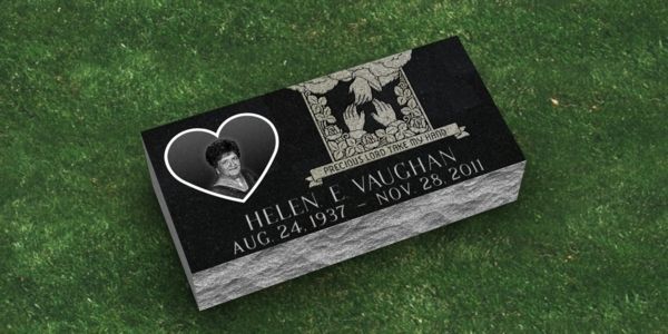 A black gravestone with a heart on it is sitting on top of a lush green field.