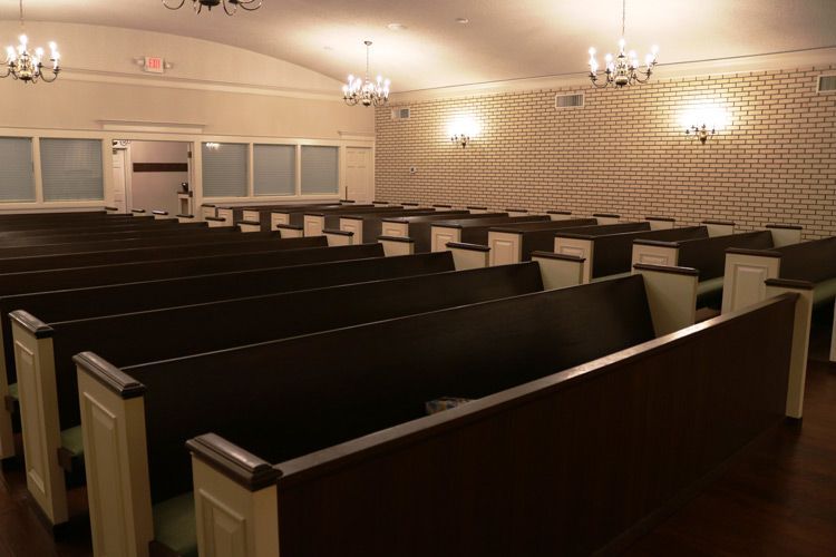 An empty church with rows of wooden benches and chandeliers hanging from the ceiling.