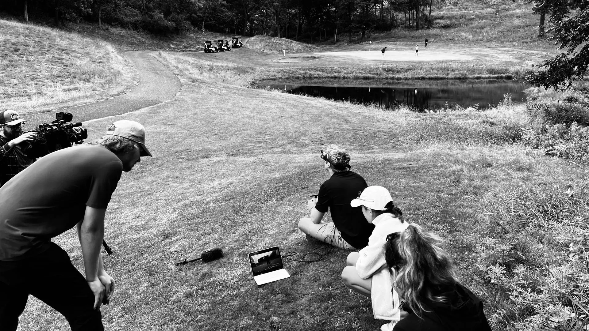 A group of people are sitting on the grass watching a golf course.