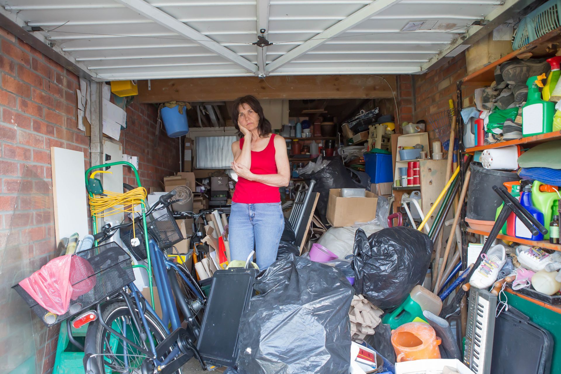 A woman is standing in a garage filled with lots of stuff.