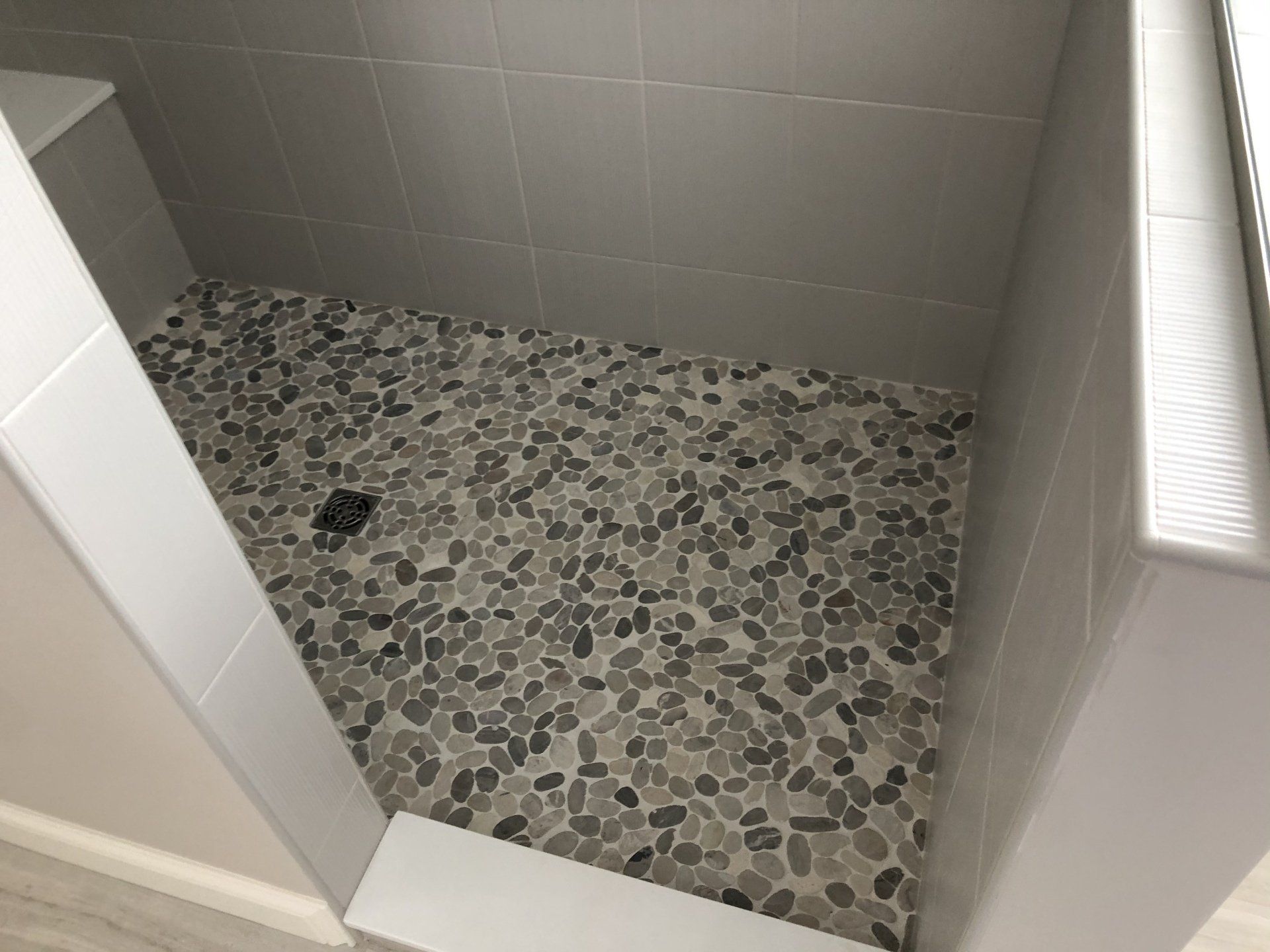 A walk in shower with a tiled floor and a window.