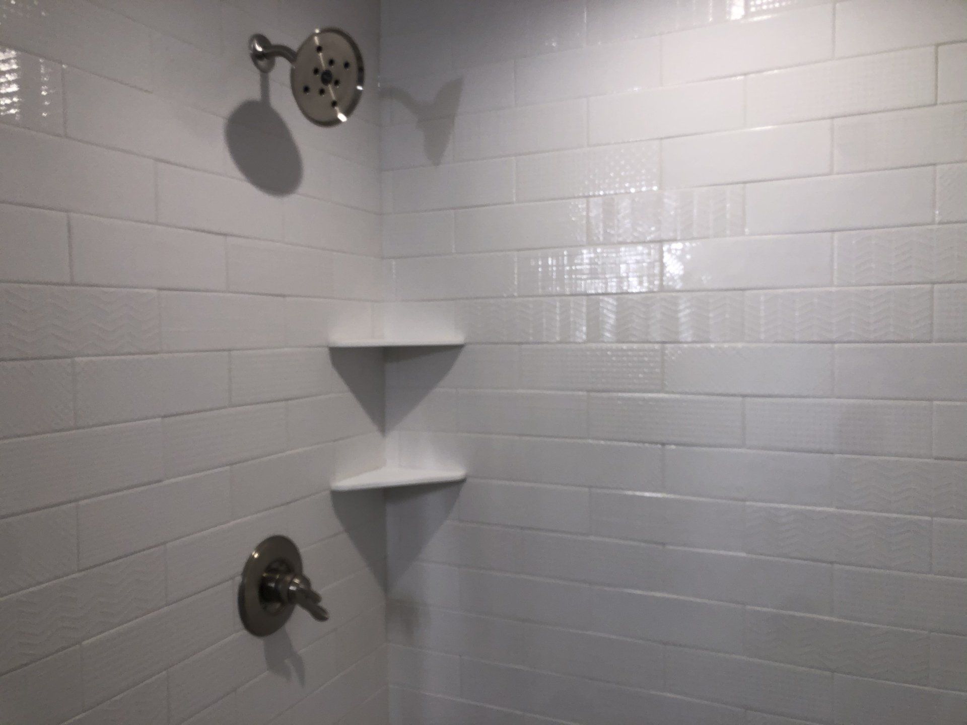 A shower with white tiles and shelves and a shower head.