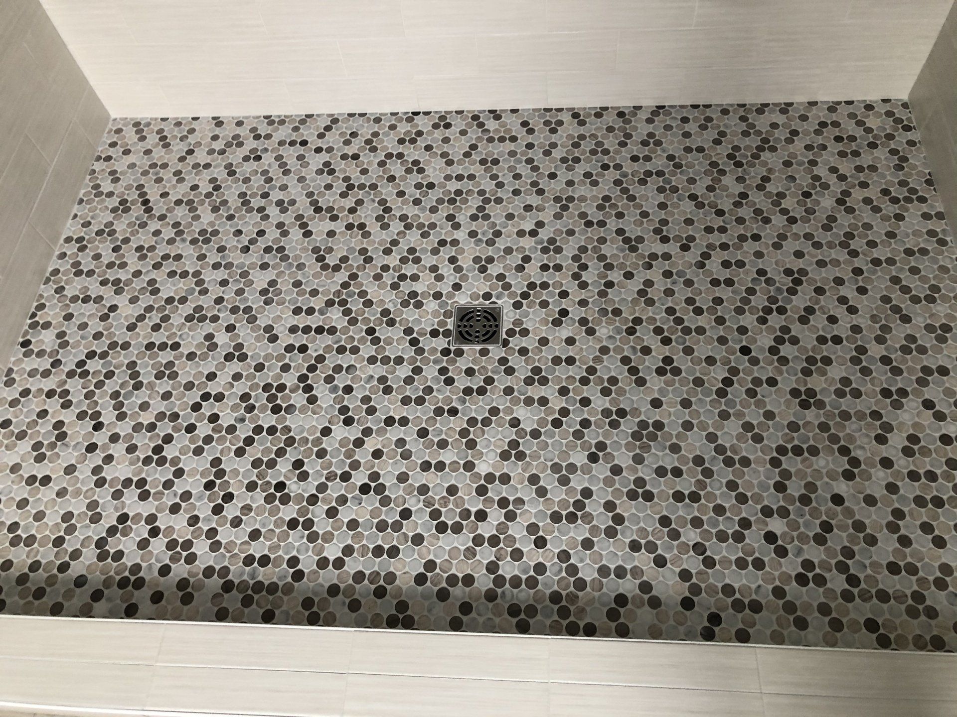 A shower stall with a mosaic tile floor and a black drain.