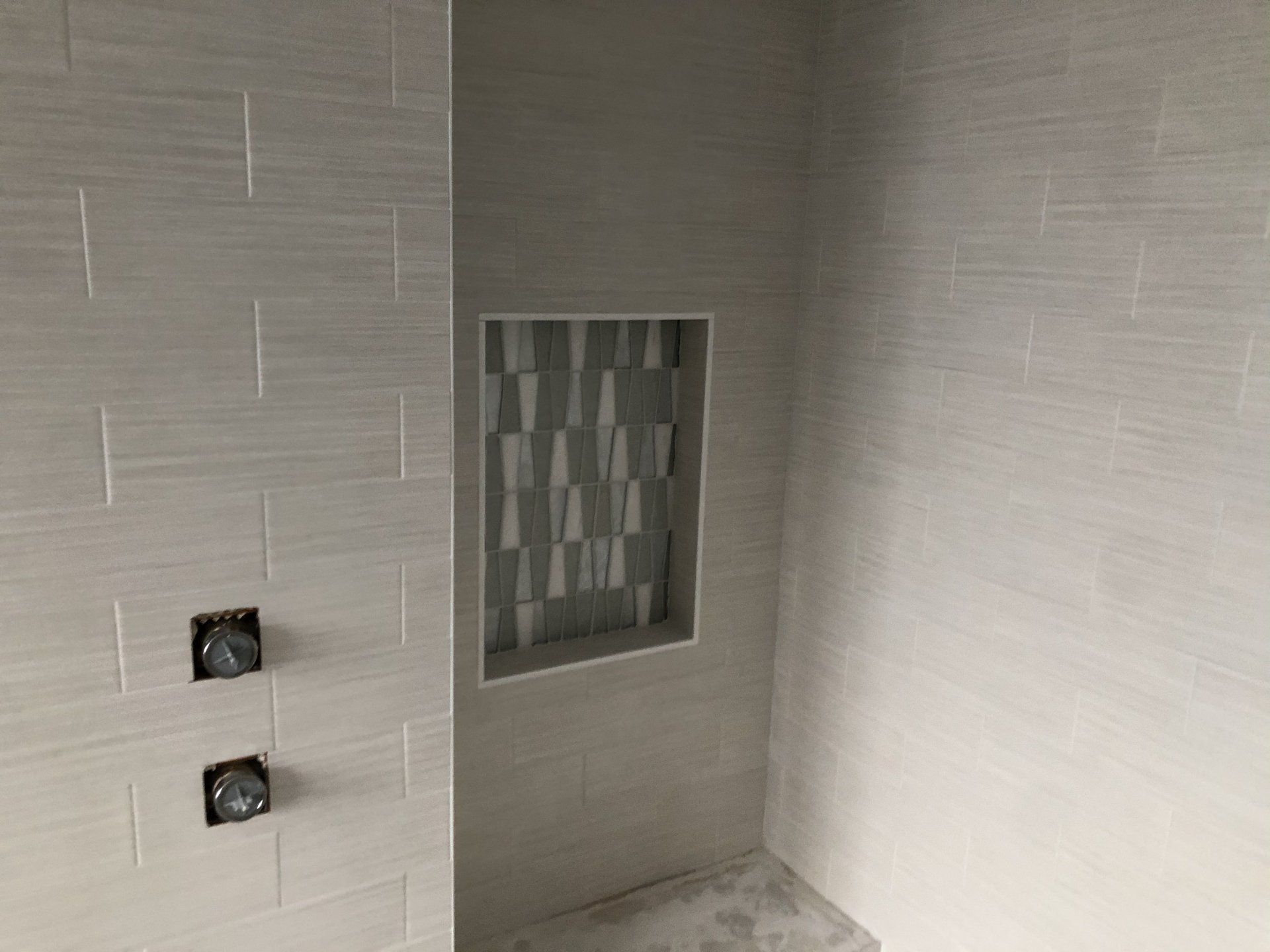 A shower stall with a built in shelf and two shower heads.