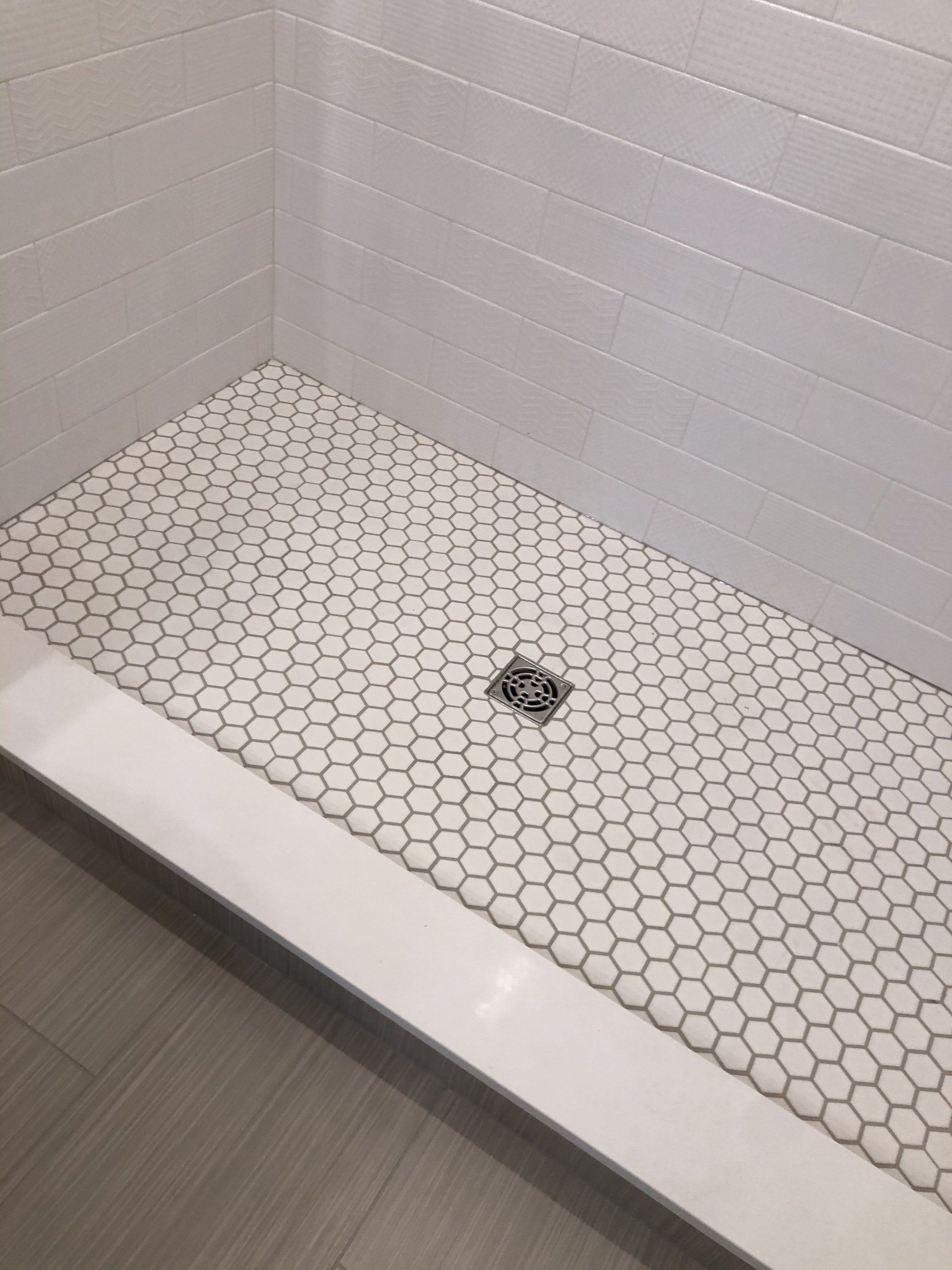 A shower stall with white tiles and a drain.
