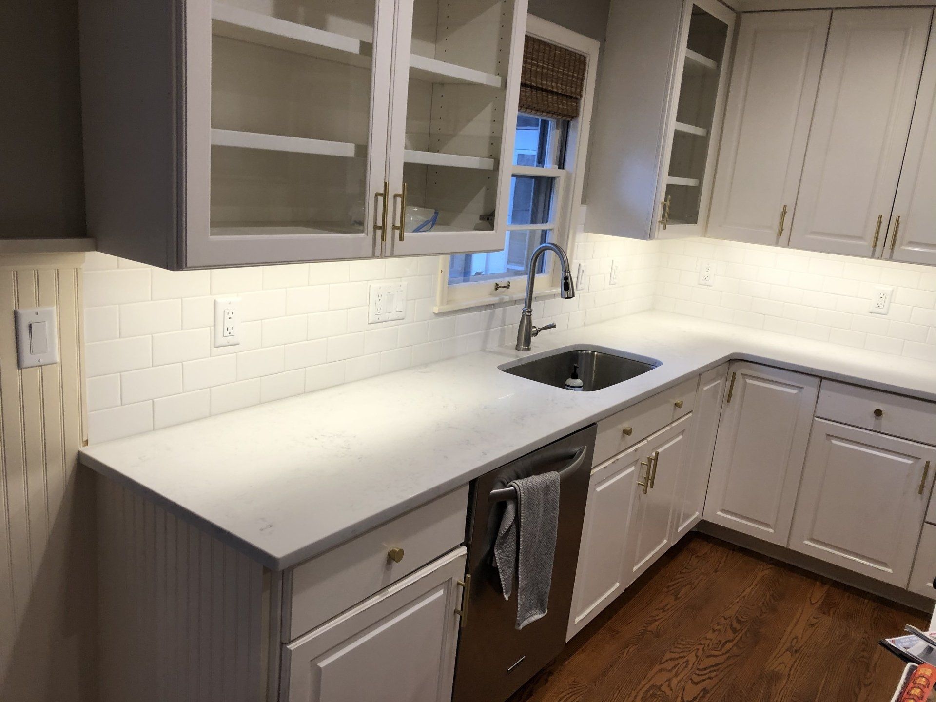 A kitchen with white cabinets , a sink , a dishwasher , and a window.