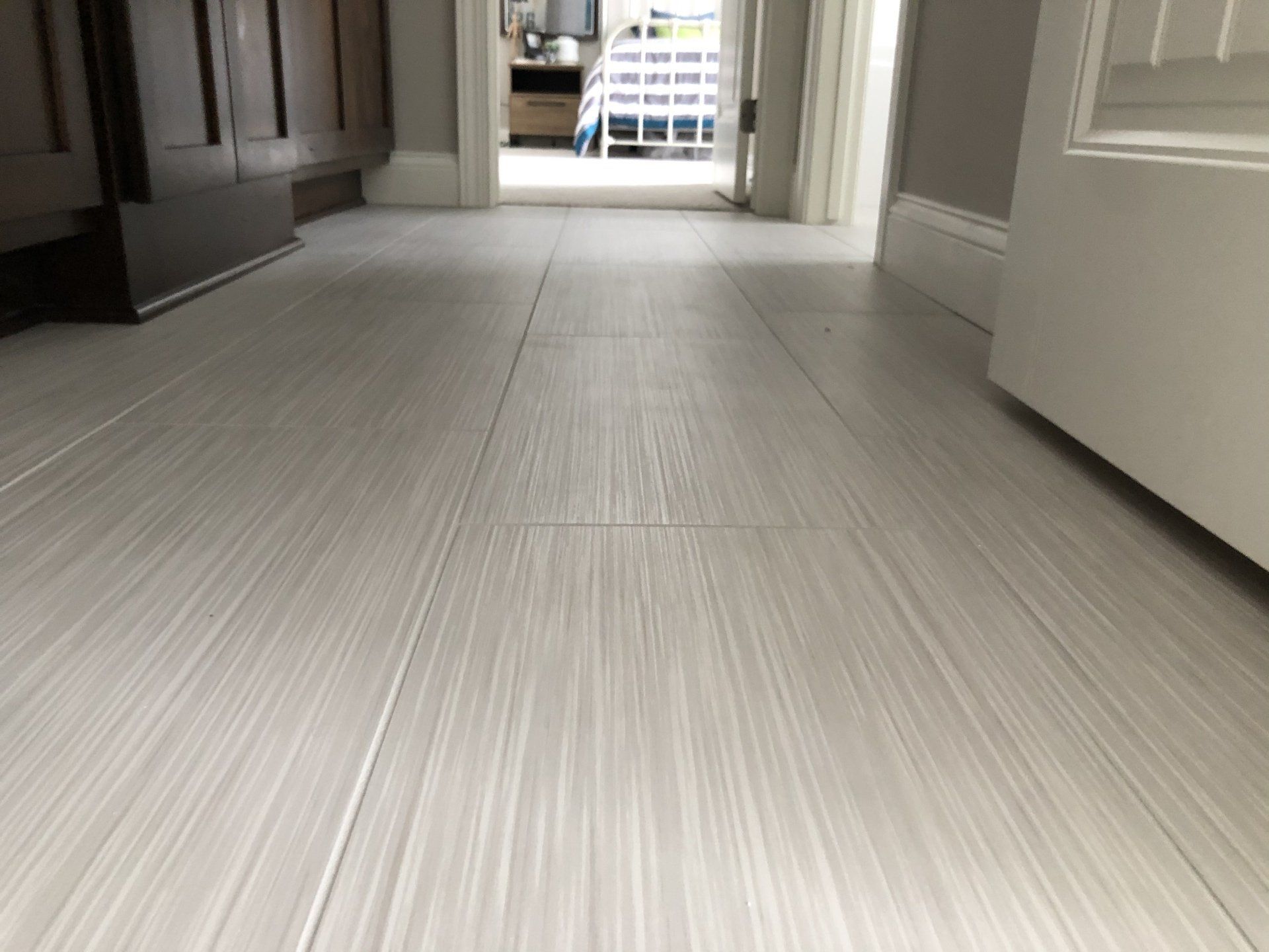 Bathroom floor tile installation | A white tile floor in a hallway leading to a bathroom.