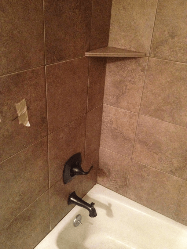 A bathtub in a bathroom with brown tiles and a corner shelf.