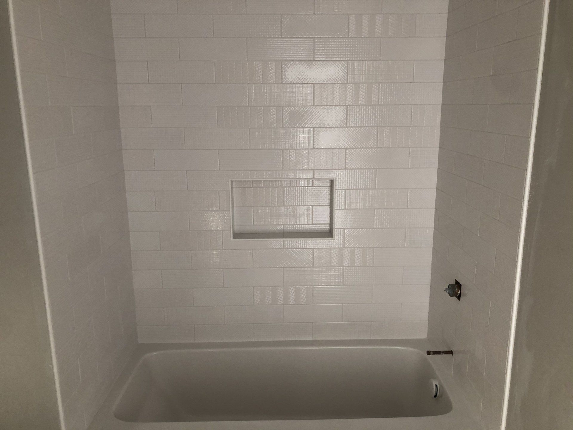 A bathtub in a bathroom with white tiles on the wall.