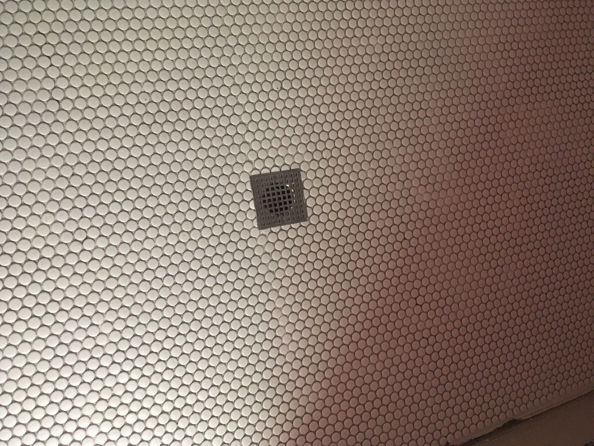 A tiled wall with a drain on it.