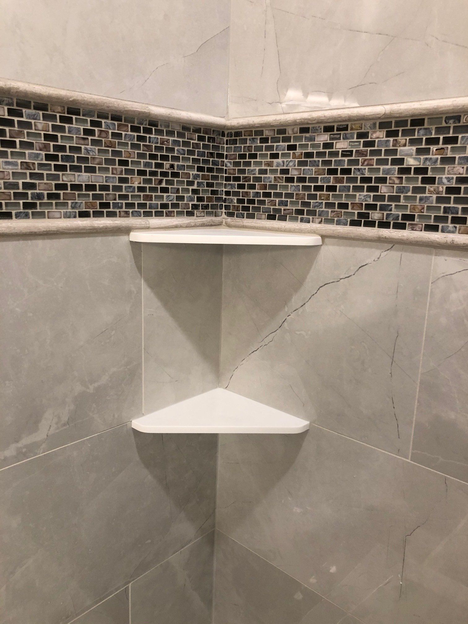 There is a corner shelf in the tiled shower with a mosaic tile border.