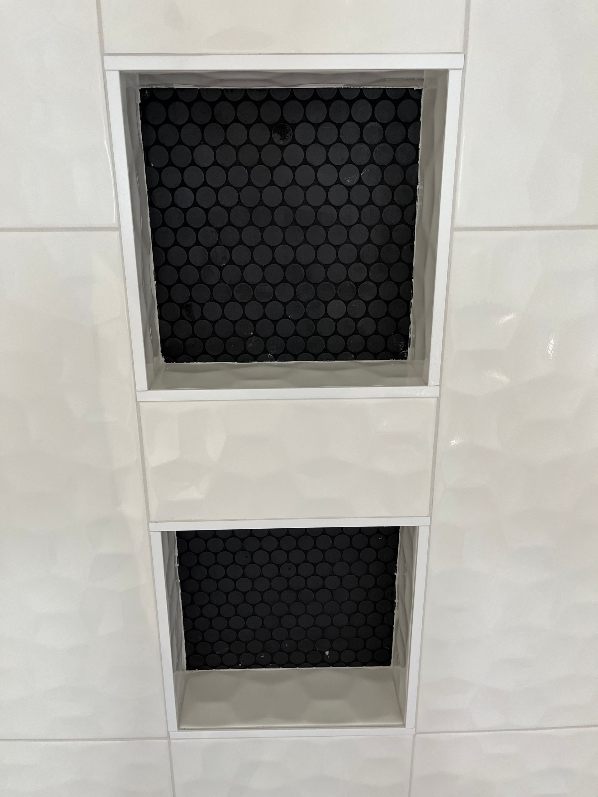A close up of a shower niche in a bathroom with black tiles.