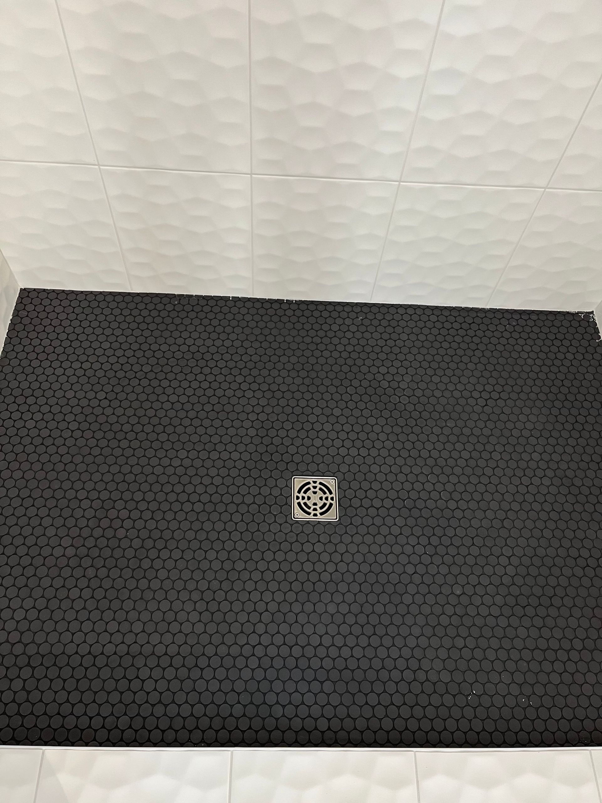 A shower stall with a black tile floor and a drain.