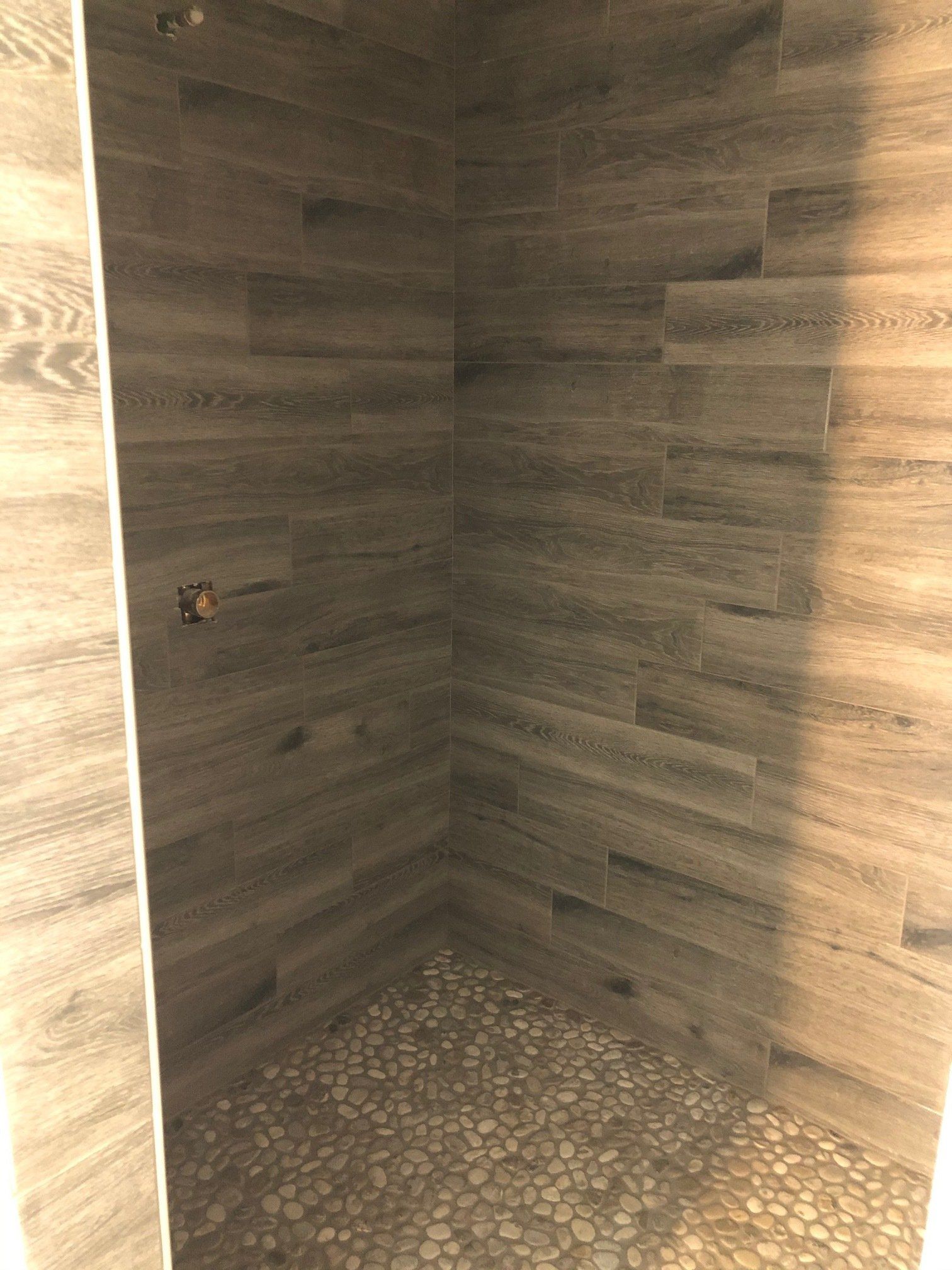 A shower renovation with wooden tiles and a pebble floor.