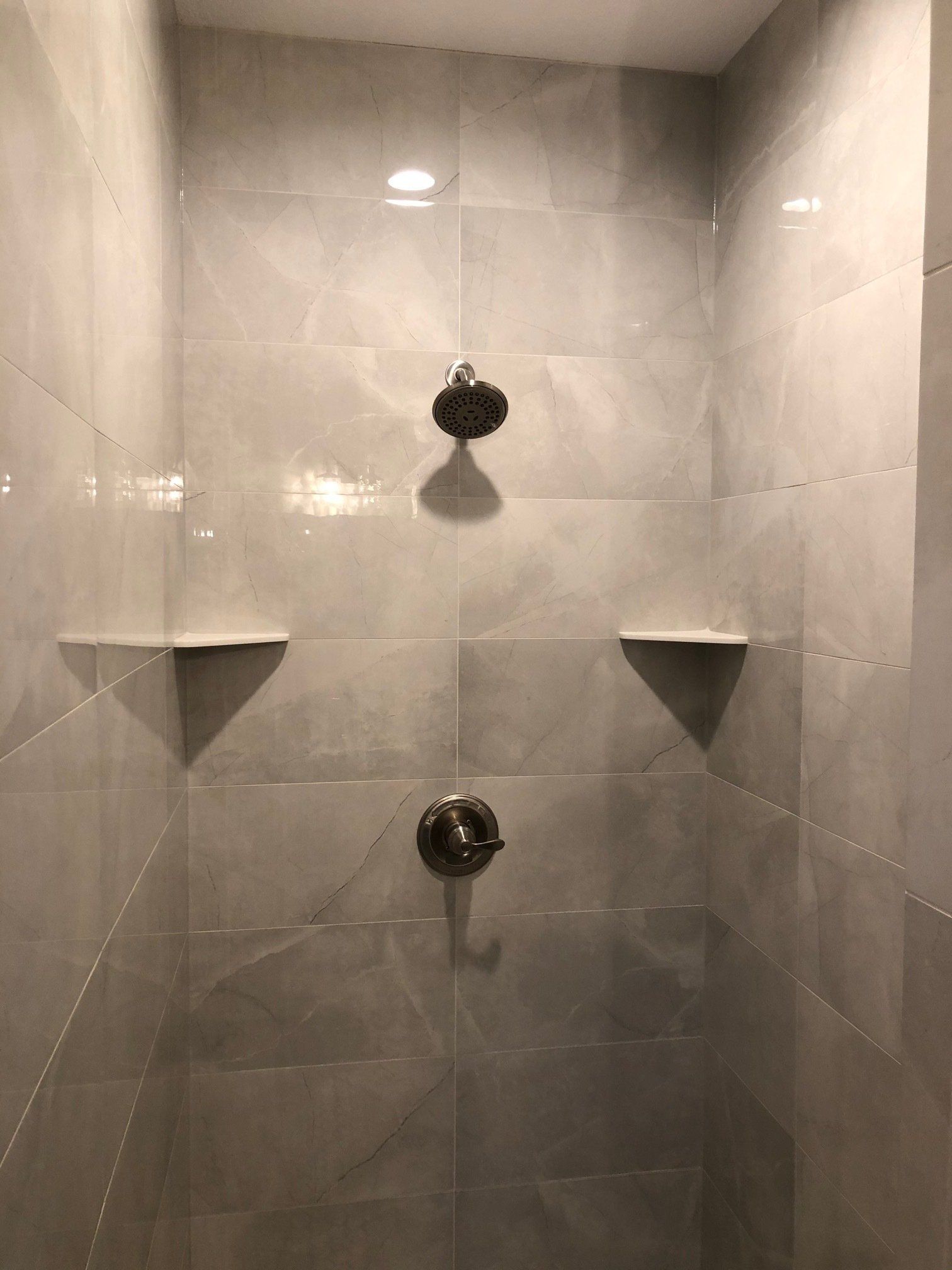 A tile shower with two shower heads and two shelves.