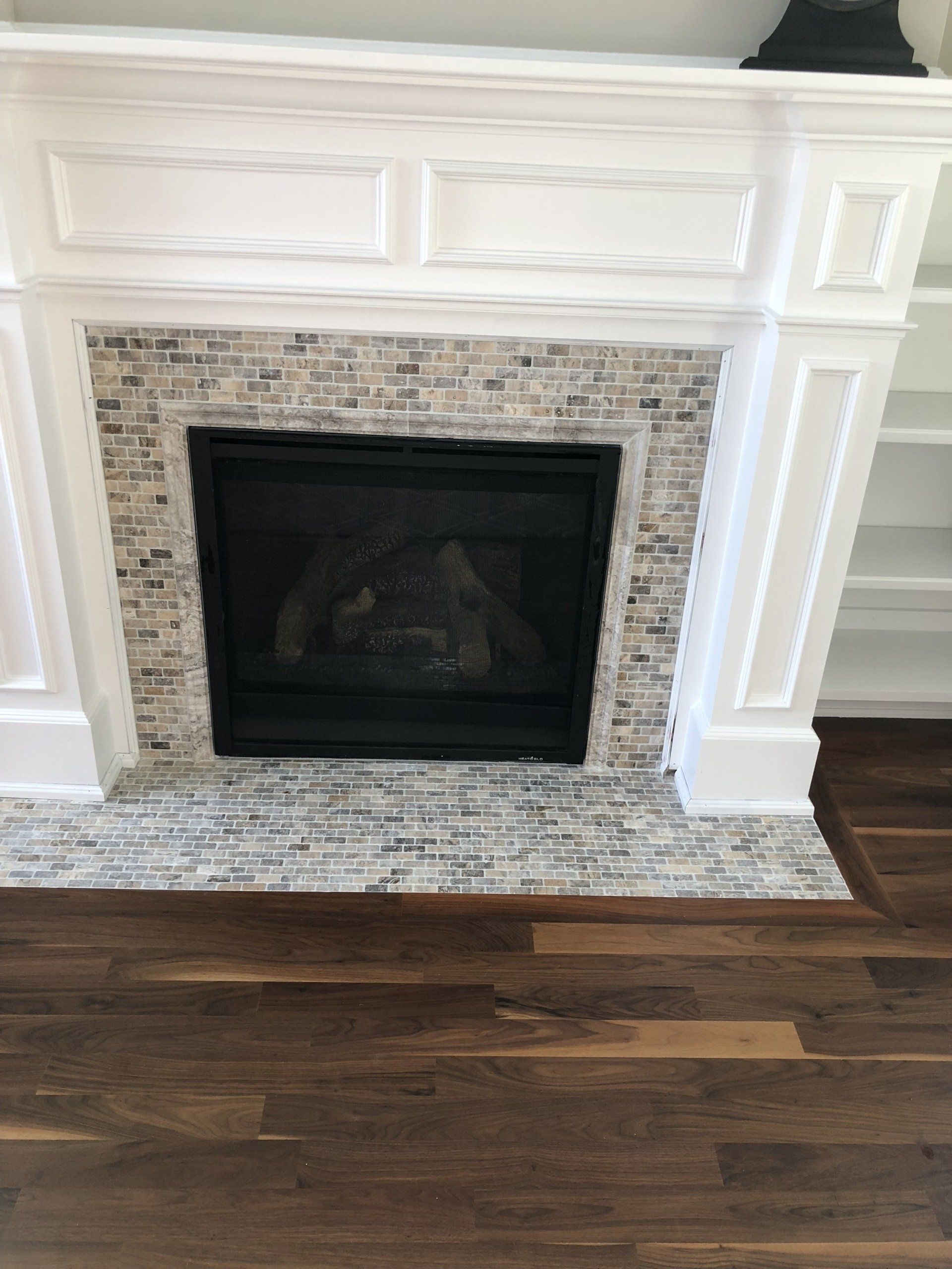 A fireplace with a tiled mantle and a wooden floor in a living room.
